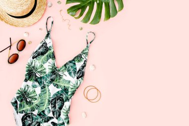 Kadın plaj aksesuarları: tropik baskılı mayo, pembe arka planda hasır şapka. Yaz dönemi. Düz yatıyordu