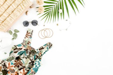 Kadın, yaz sokak tarzı. Elbise, hasır şapka, spor ayakkabı, güneş gözlüğü ve tropikal yaprak. Üst manzara, düz uzanma.