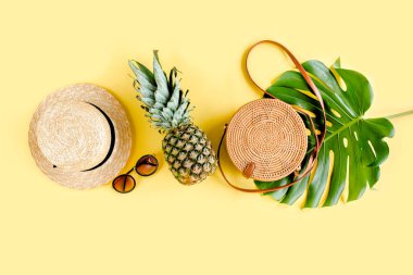 Kadın aksesuar gezgini: bambu çanta, hasır şapka, tropik palmiye yaprakları canavarı, sarı arka planda retro kamera. Düz yatış, üst görünüm