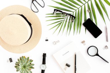 Üst kat ofis masası. Hasır şapka, gözlük, retro kamera, not defteri ve beyaz arka planda tropikal palmiye yaprağı olan çalışma alanı. Düz yatış, üst görünüm.