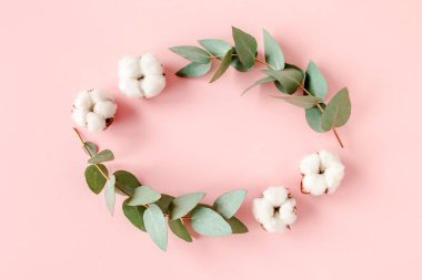 Çiçek bileşimi, okaliptüs dallarından yapılmış çelenk, pembe arka planda izole edilmiş yapraklar ve pamuk. Düz bir zemin, üst manzara. Çiçek konsepti