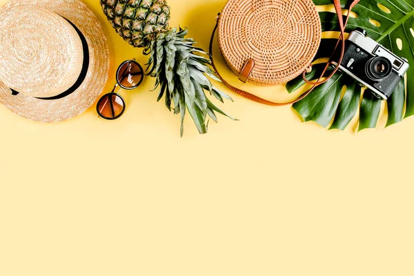 Accesorios mujer viajero: bolsa de bambú, sombrero de paja, hojas de palma tropical monstera, cámara retro sobre fondo amarillo. Piso tendido, vista superior — Foto de Stock