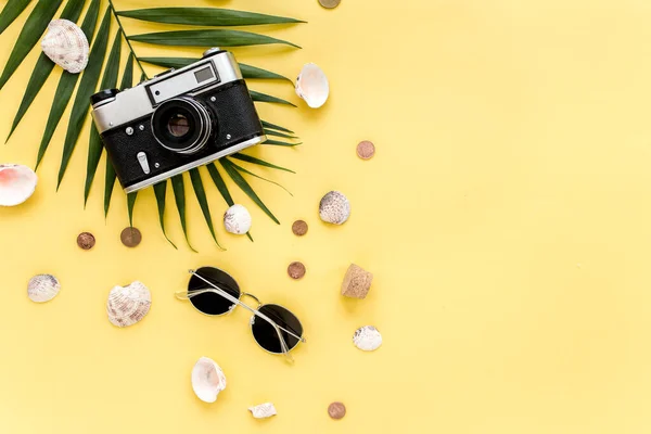 Аксессуары для путешественников на желтом фоне с пальмовым листом, фотоаппаратом и солнцезащитными очками. Квартира лежала, вид сверху. Летний фон. — стоковое фото