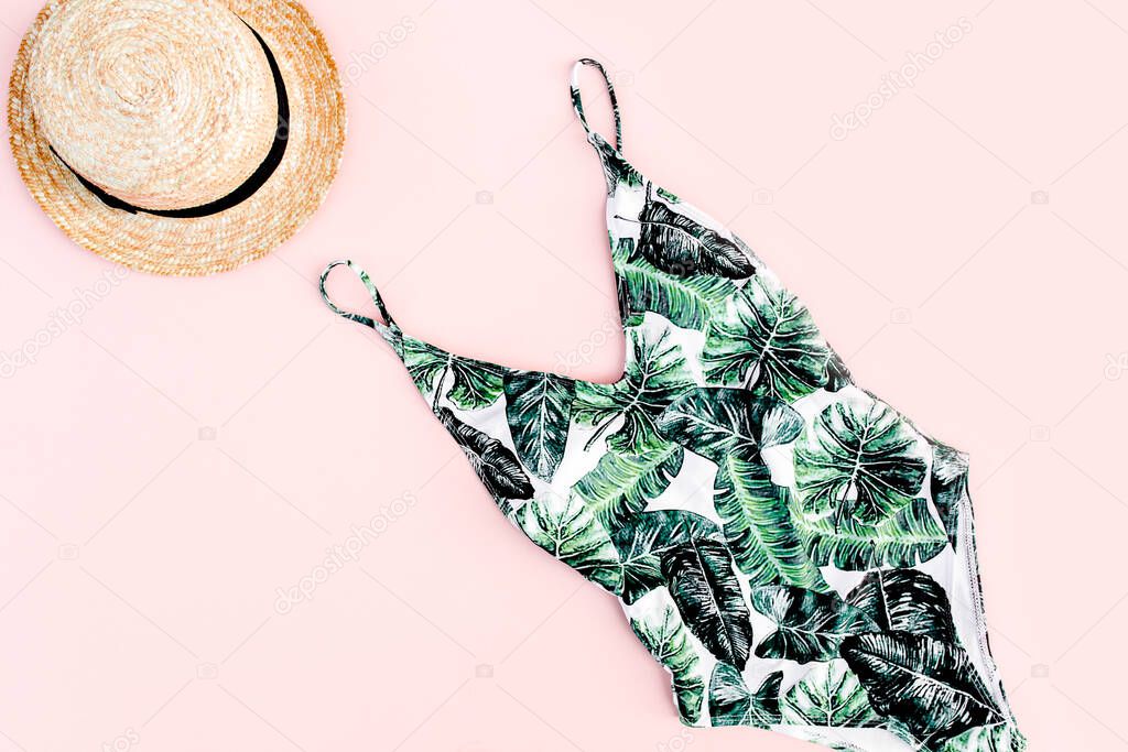 Womans beach accessories: swimsuit with tropical print, straw hat on pink background. Summer background. Flat lay