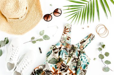 Kadın, yaz sokak tarzı. Elbise, hasır şapka, spor ayakkabı, güneş gözlüğü ve tropikal yaprak. Üst manzara, düz uzanma.