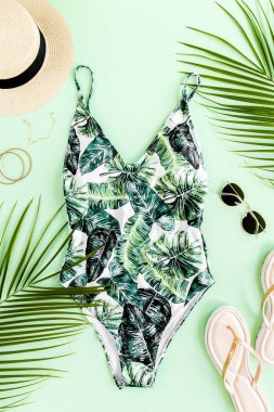 Kadın plaj aksesuarları: bikini, rattan çanta, hasır şapka, sarı arka planda tropik palmiye yaprakları. Yaz arkaplanı. 