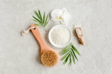 Spa konsepti. Doğal organik spa ürünleri, deniz tuzu, masaj fırçası ve yukarıdaki gri mermer masada tropik palmiye yaprakları. Spa arkaplanı