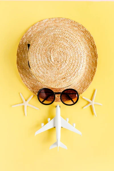 Туристическое лицо из соломенной шляпы, модели самолета, самолета и солнцезащитных очков на желтом фоне. Концепция принадлежностей. — стоковое фото