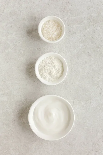 Три различных натуральных косметических средства в миске: крем для лица, косметическая глина, морская соль на сером мраморном фоне. Концепция Skincare. — стоковое фото