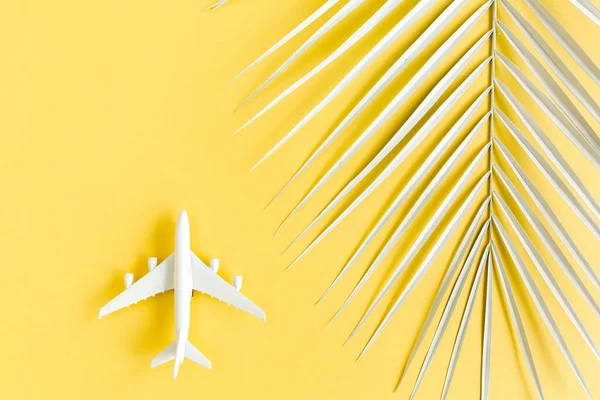 Plano modelo branco, avião e folha de palma sobre fundo amarelo. Vista superior, deitado plano. Viagens, conceito de férias. — Fotografia de Stock