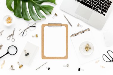 Ev ofisinin çalışma alanı dizüstü bilgisayarı, tropikal yaprakları Monstera, not panosu, defter ve aksesuarları beyaz arka planda. Düz yatış, üst görünüm