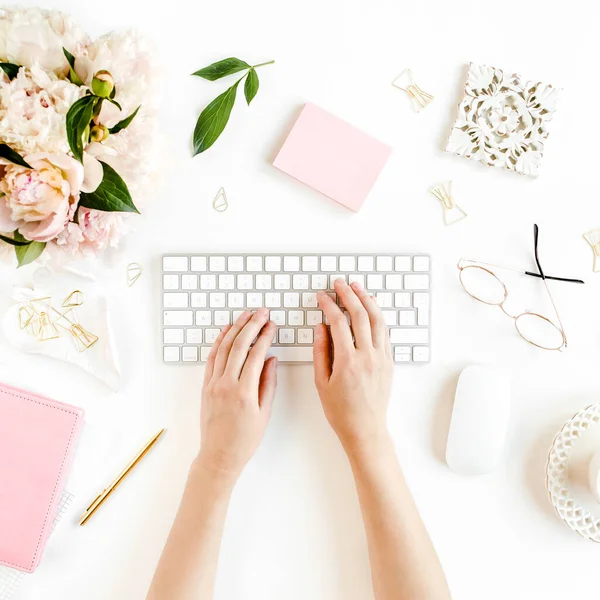 Scrivania da ufficio per donne piatte. Spazio di lavoro femminile con mani femminili, computer, bouquet di peonie rosa, accessori su sfondo bianco. Vista dall'alto. — Foto Stock