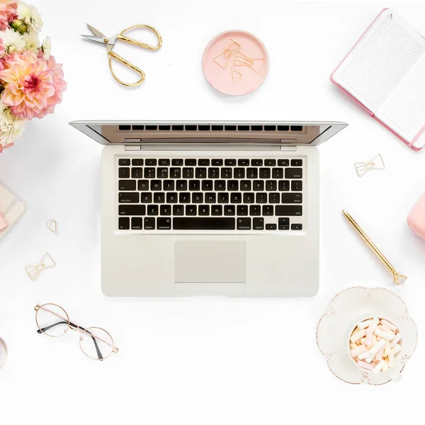 Stylized womens home office desk. Workspace with laptop, computer, bouquet ranunculus and roses, clipboard on white background. Flat lay. Top view.