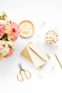 Ev ofisinin masası düzdü. Pembe güllü kadın çalışma alanı, yıldız çiçeği buketi, altın aksesuarlar, beyaz arka planda günlük. Üst görünüm.