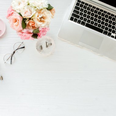 Düz uzanmış kadınların ofis masası. Dizüstü bilgisayarı, pembe gülleri, çiçekleri, aksesuarları, günlüğü, beyaz tahta arka planda gözlüğü olan kadın çalışma alanı. Üst görünüm.