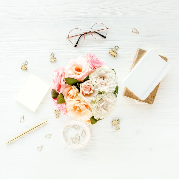 Pembe güller, çiçek buketleri, aksesuarlar, altın günlük, beyaz ahşap arka planda gözlük. Üst görünüm