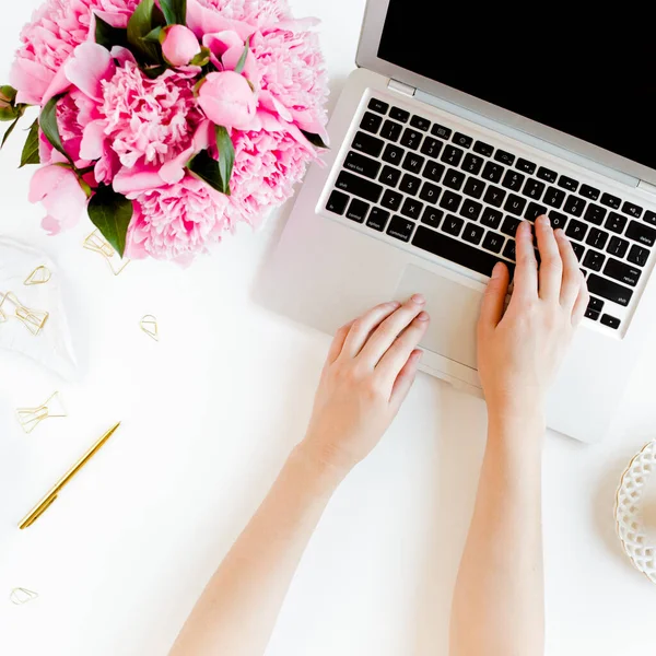 Espacio de trabajo femenino con manos femeninas, portátil, ramo de peonías rosadas, accesorios sobre fondo blanco. Vista superior de fondo femenino. Puesta plana. —  Fotos de Stock