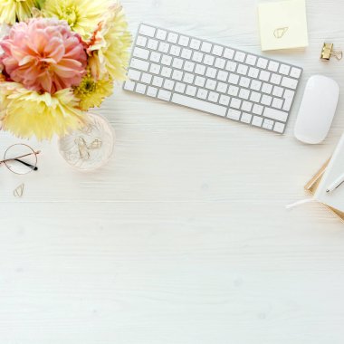 Düz uzanmış kadınların ofis masası. Bilgisayarlı kadın çalışma alanı, pembe ve sarı güller çiçekler, aksesuarlar, günlük, beyaz arka planda gözlük. Üst görünüm