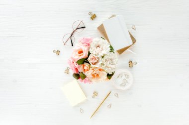 Pembe güller, çiçek buketleri, aksesuarlar, altın günlük, beyaz ahşap arka planda gözlük. Üst görünüm