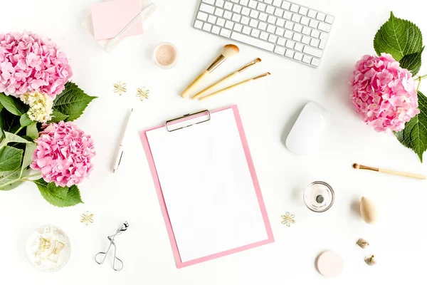 Meja wanita yang bergaya. Ruang kerja dengan papan klip, komputer, bouquet hydrangea, aksesoris pada latar belakang putih. Berbaringlah. Tampilan atas. — Stok Foto