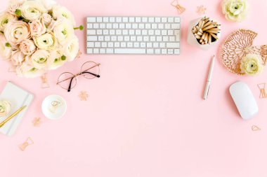 Tarz sahibi, pembe kadınların ofis masası. Bilgisayarlı çalışma alanı, buket ranunculus ve güller, pembe arka planda pano. Düz yatıyordu. Üst görünüm.