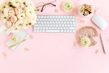 Tarz sahibi, pembe kadınların ofis masası. Bilgisayarlı çalışma alanı, buket ranunculus ve güller, pembe arka planda pano. Düz yatıyordu. Üst görünüm.
