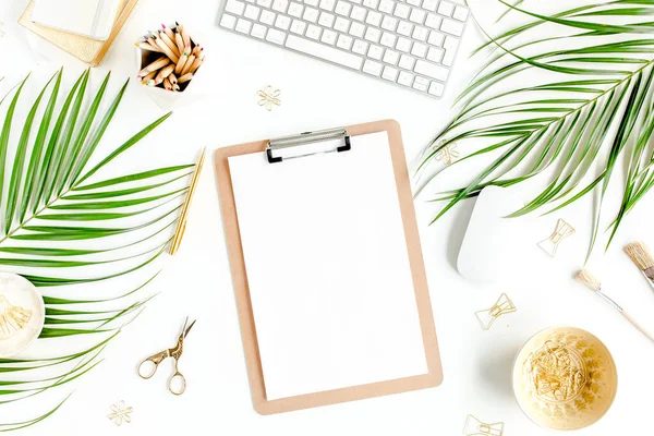 Flat lay mesa de escritório em casa. Espaço de trabalho feminino com computador, área de transferência, folhas de palma tropicais, acessórios sobre fundo branco. Vista superior. — Fotografia de Stock