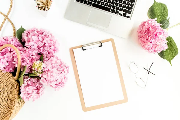 Meja wanita yang bergaya. Ruang kerja dengan papan klip, laptop, bouquet hydrangea, aksesoris pada latar belakang putih. Berbaringlah. Tampilan atas. — Stok Foto