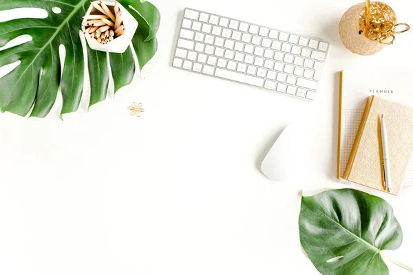Female office desk workspace with computer, tropical palm leaves Monstera, accessories on white background. Top view feminine background.