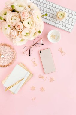 Tarz sahibi, pembe kadınların ofis masası. Bilgisayarlı çalışma alanı, buket ranunculus ve güller, pembe arka planda telefon. Düz yatıyordu. Üst görünüm.