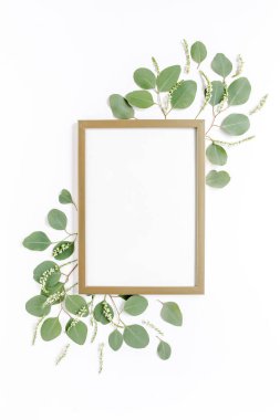 Kare altın çerçeve, yeşil okaliptüs yaprakları, dallar, beyaz arka planda çiçek desenleri ile süslenmiş. Daire üst manzaralı. Çiçek çerçevesi. 