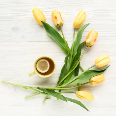 Sarı laleler, beyaz, ahşap arka planda izole edilmiş bir fincan çay. Düz uzan, üst görünüm