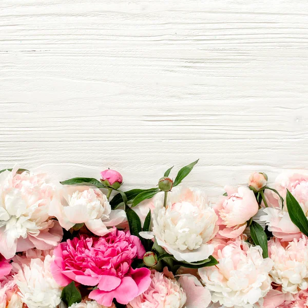 Ghirlanda a cornice floreale composta da boccioli di fiori di peonie rosa e beige, rami di eucalipto e foglie isolate su fondo bianco in legno. Posa piatta, vista dall'alto — Foto Stock