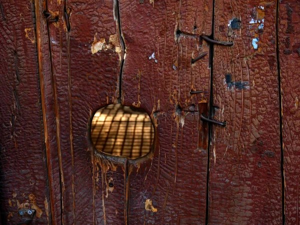마당을 들여다볼 수있는 구멍 이 있는 오래 된 나무로 된 문 — 스톡 사진