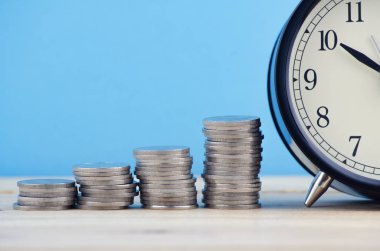 Para kavramı, yığın sikke ve çalar saat ahşap masa üzerinde tam zamanı