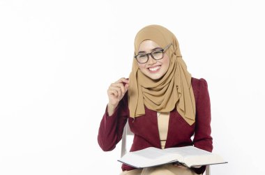 Oturma ve beyaz arka plan üzerinde kitap hijab ile kendine güvenen genç kadın.