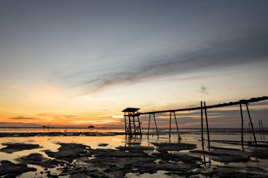 Altın saat an, güzel tropikal günbatımı arka plan, ahşap su pompası Kulesi çamurlu sahilde. bulutlu ve sarı sky.surface düzey shot.low gelgit deniz manzaralı