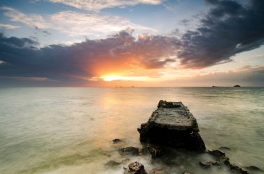 çarpıcı görüntü günbatımı sahil şeridi boyunca. beton yapı su, güneş ışığı ile dramatik kara bulutlar terk.
