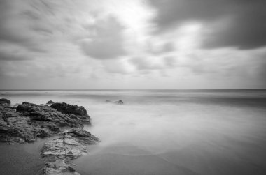 siyah beyaz resim, kumlu plaja karanlık bulut arka plan üzerinde isabet dalga yumuşak akışı. uzun pozlama ateş nedeniyle yumuşak odak görüntü