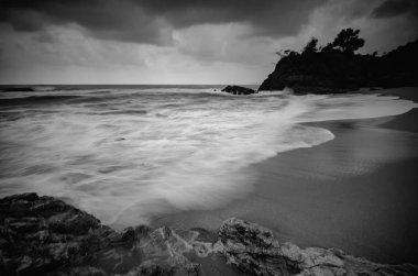 siyah beyaz resim, kumlu plaja karanlık bulut arka plan üzerinde isabet dalga yumuşak akışı. uzun pozlama ateş nedeniyle yumuşak odak görüntü