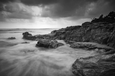 siyah beyaz resim, kumlu plaja karanlık bulut arka plan üzerinde isabet dalga yumuşak akışı. uzun pozlama ateş nedeniyle yumuşak odak görüntü
