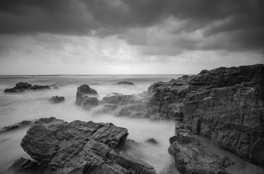siyah beyaz resim, kumlu plaja karanlık bulut arka plan üzerinde isabet dalga yumuşak akışı. uzun pozlama ateş nedeniyle yumuşak odak görüntü