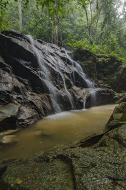 bulanık ve seçici odak resim yeşil orman güneş ışığı etkisi ile. dağdan aşağı düşen güzel tropik şelale. Yeşil yosunlu kayanın üzerinde