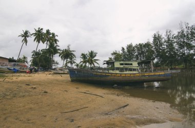 Kumsalda karaya ahşap gemi enkazı. bulutlu gökyüzü ve yeşil ağaç arka plan