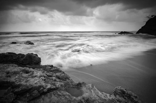 black and white image,beautiful tropical wave flow hitting the sandy beach over dark cloud background. soft focus image due to long exposure shot