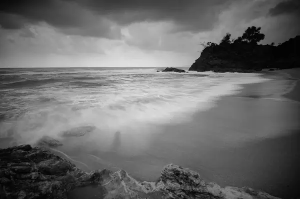 black and white image,stunning tropical wave flow hitting the sandy beach over dark cloud background. soft focus image due to long exposure shot