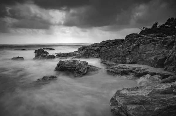 siyah beyaz resim, kumlu plaja karanlık bulut arka plan üzerinde isabet dalga yumuşak akışı. uzun pozlama ateş nedeniyle yumuşak odak görüntü
