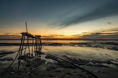 Altın saat an, güzel tropikal günbatımı arka plan, ahşap su pompası Kulesi çamurlu sahilde. bulutlu ve sarı sky.surface düzey shot.low gelgit deniz manzaralı