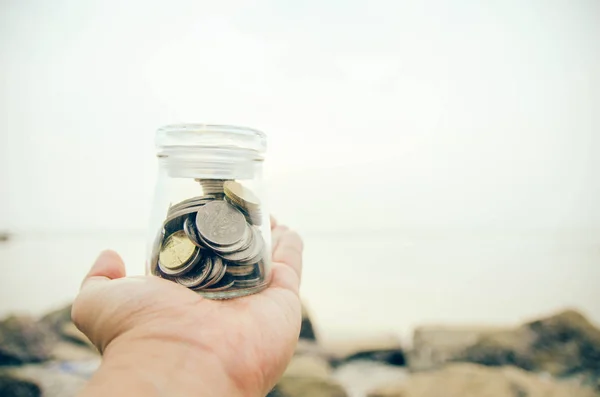 selective focus and blurred image hand holding glass jar contain with coin at the beach. blur background during sunset at the beach