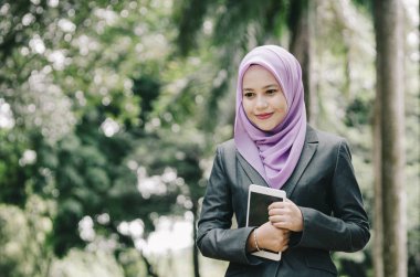 Öğrenci ve iş kavramı, ayakta ve tablet tutan kentsel park arka plan üzerinde takım elbiseli Genç profesyonel hijab kadınlar.
